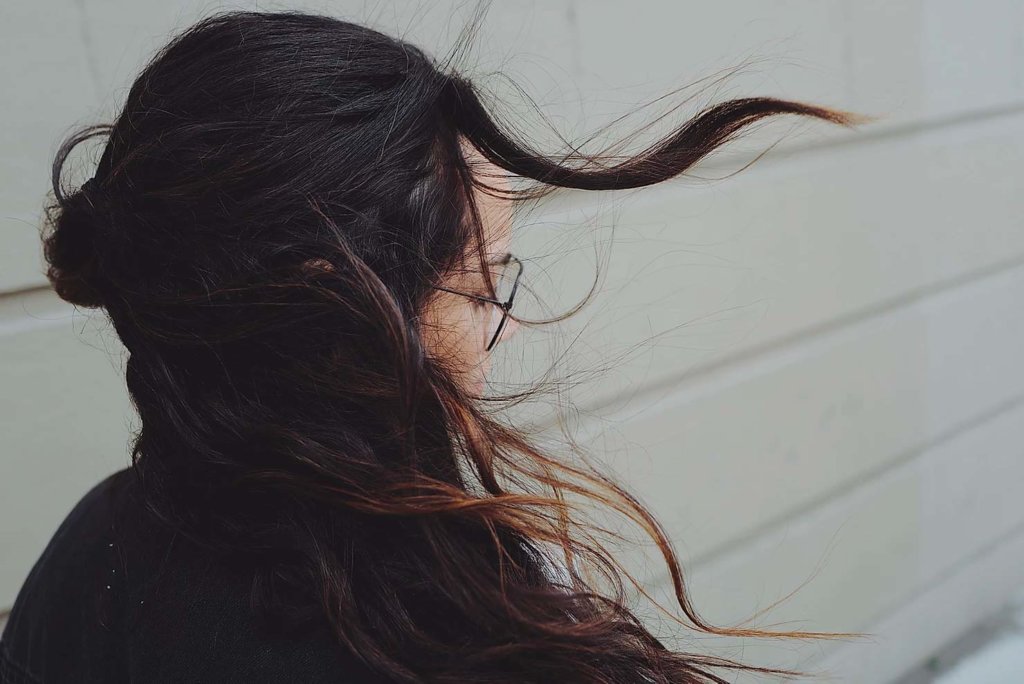 Woman wearing glasses with dark hair that is blowing in the wind.