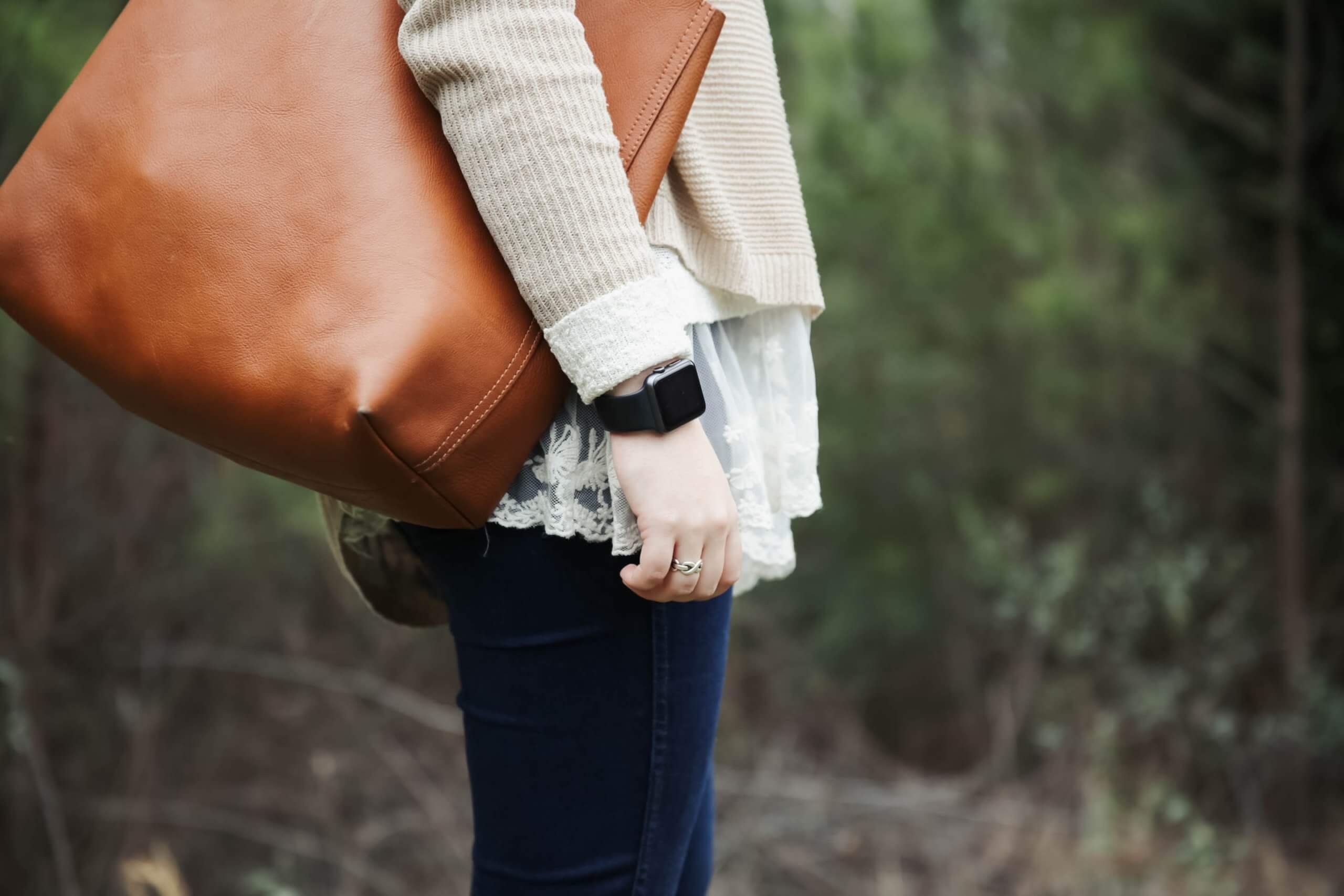 A woman wearing an Apple Watch carrying a brown leather tote bag.