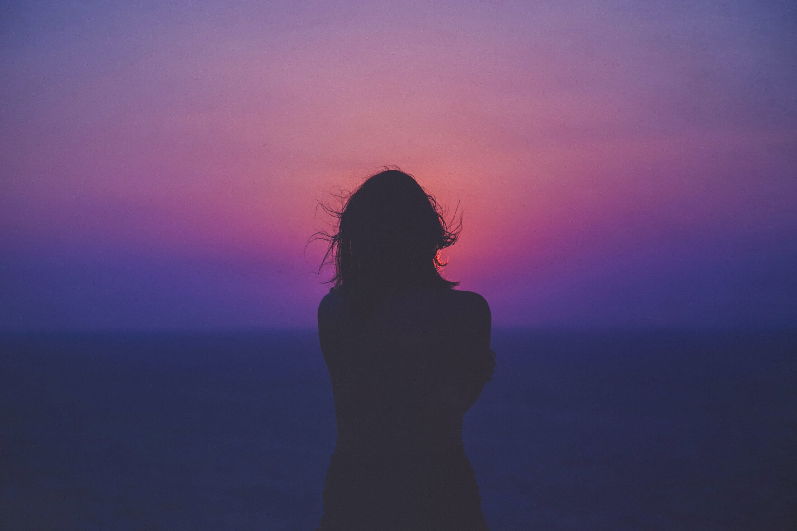 Silhouette of a woman looking at a colorful sunrise