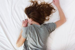 Brunette woman with itchy scalp at night laying face down on white sheets