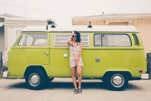 Young woman with curly hair and sunglasses standing in front of green VW van.